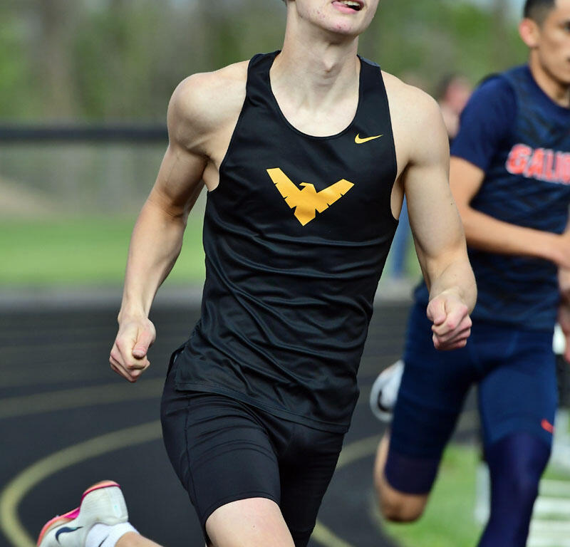 Young male sprinter in a black singlet with a gold WV logo, sprinting on an outdoor track.