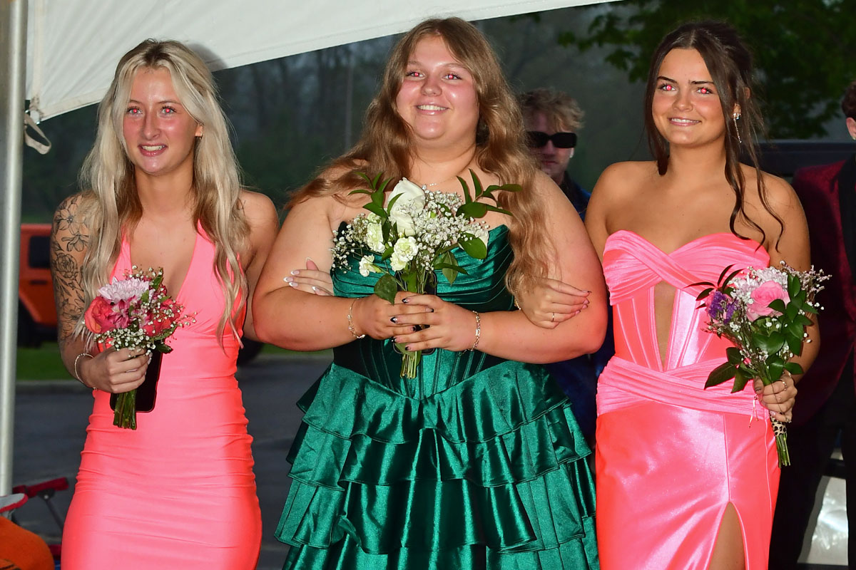 Three young women in formal dresses pose together, each holding a bouquet of flowers.