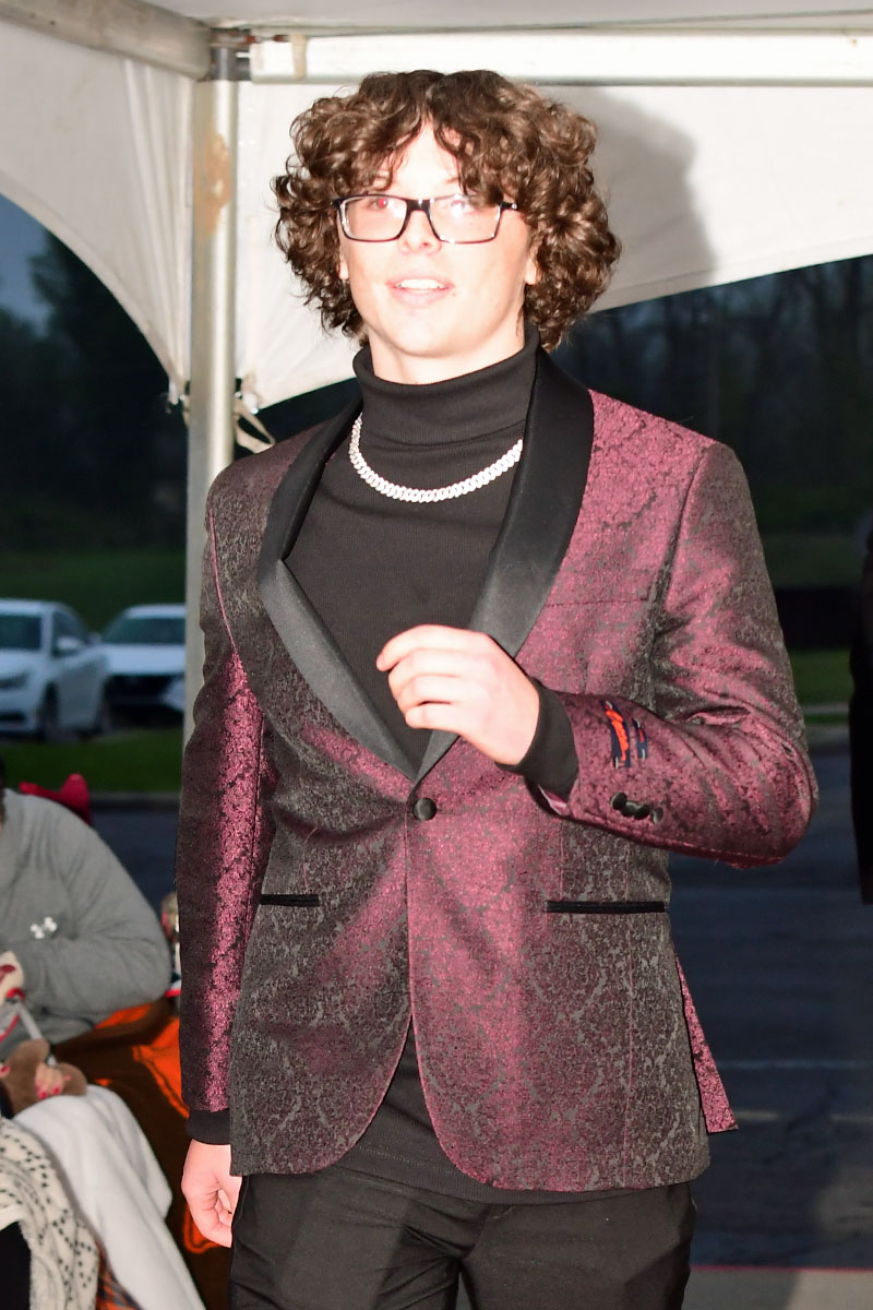Person wearing a shimmering burgundy blazer, black turtleneck, and pearl necklace at an indoor event/venue.