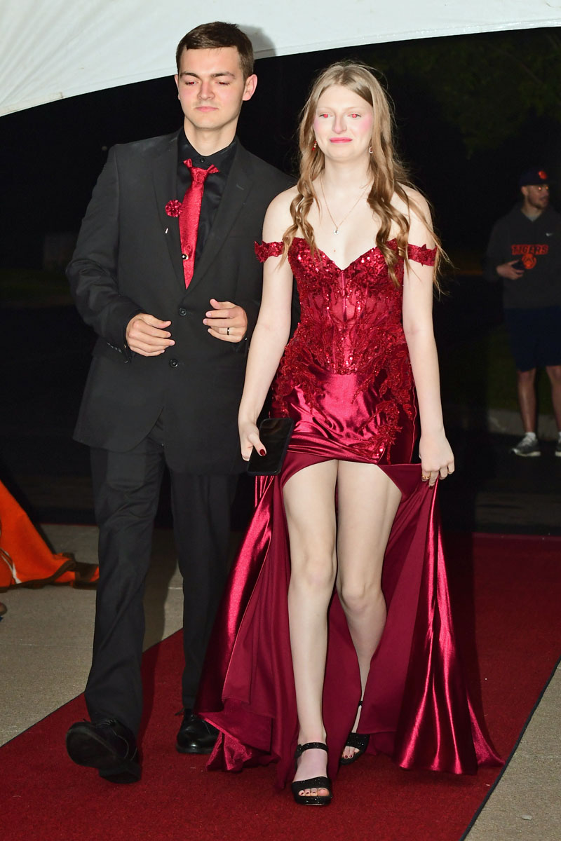 Couple walking a red carpet at night; woman in a red sequined evening gown, man in a black suit with a red tie.