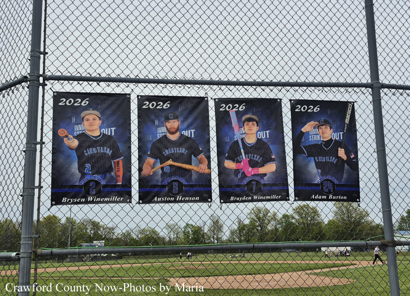 Four 2026 team banners on a chain-link fence above a baseball field, each showing a player in uniform (Brysen Winemiller, Auston Henson, Brayden Winemiller, Adam Burton) with a bat or glove.