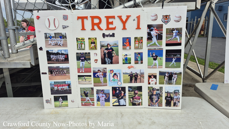 White display board titled 'TREY 1' featuring many small baseball photos arranged as a collage at a baseball field.",