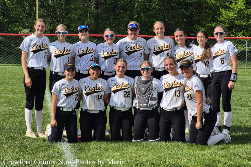 Girls softball team in white and gold striped uniforms posing for a group photo on a grassy field.