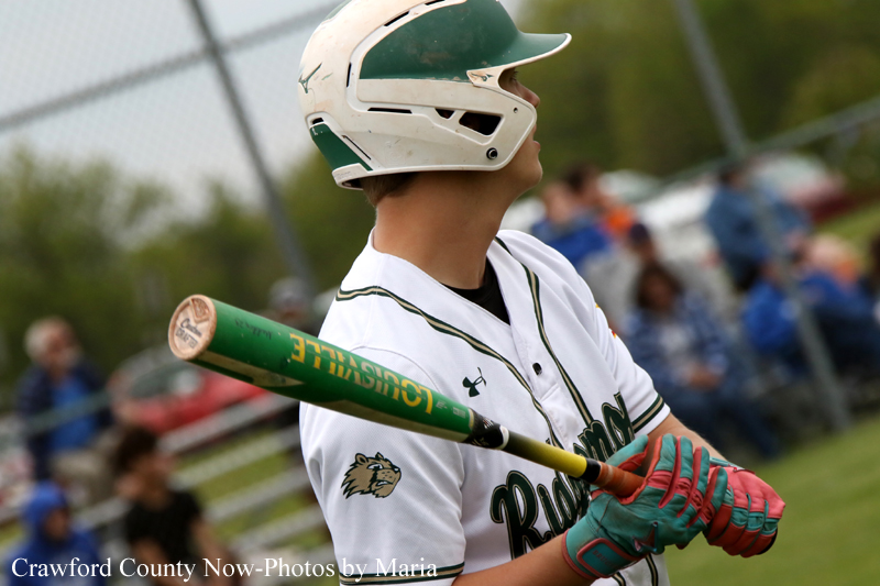 Baseball batter in a white uniform with a green helmet, gripping a green Louisville Slugger bat as he prepares to swing.