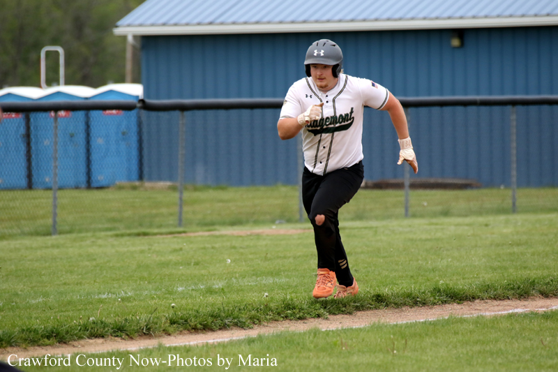 Baseball player in a white jersey and helmet sprinting along the baselines on a grassy field near a blue building.
