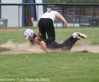 Baseball players collide as a runner slides headfirst into a base while a fielder reaches to tag, kicking up dust.