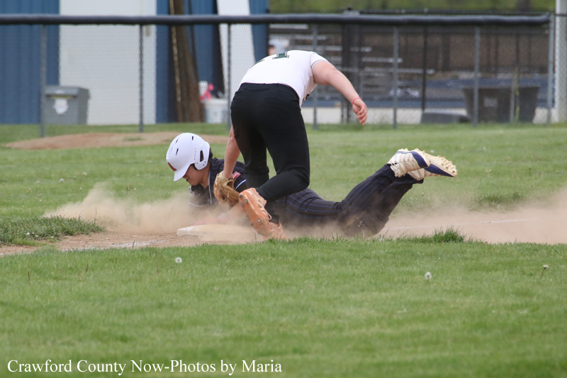 Baseball players collide as a runner slides headfirst into a base while a fielder reaches to tag, kicking up dust.