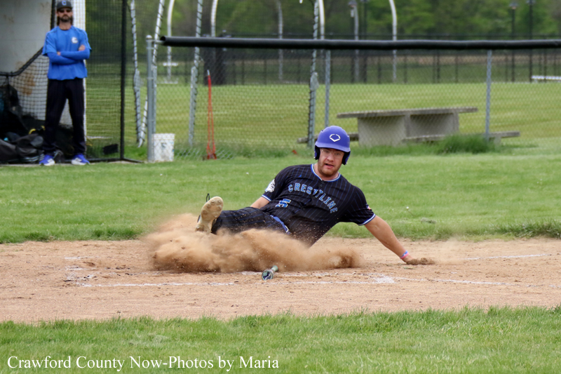Baseball player in a dark uniform slides into a base, kicking up a cloud of dirt during a game.