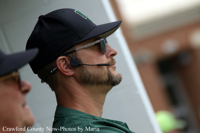 Man wearing a black cap, sunglasses, and headset microphone, looking to the right at an event.