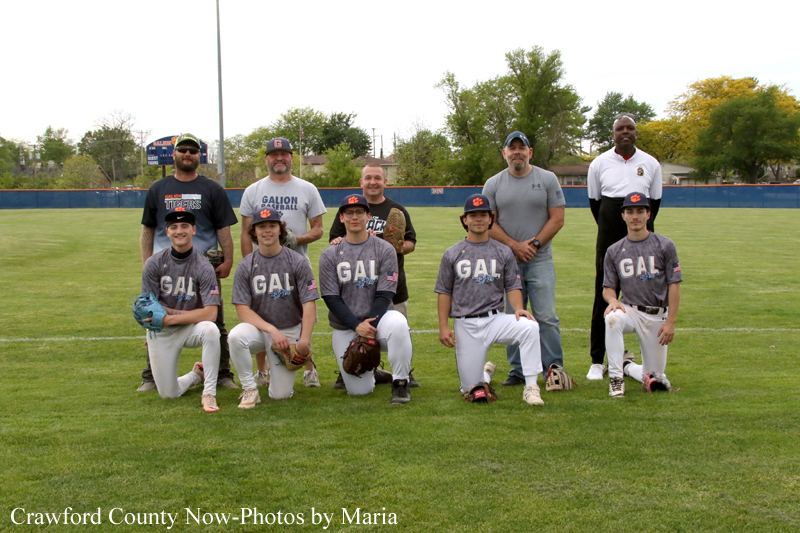 Youth baseball team and coaches pose for a group photo on a grassy field.
