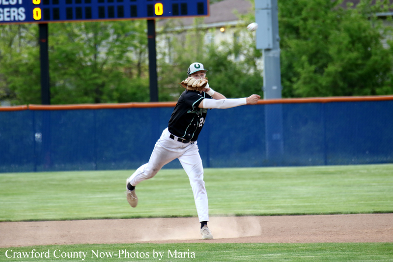 Pitcher in a black uniform throws a pitch on the baseball diamond; dust rises as his front foot lands on the dirt mound behind him.