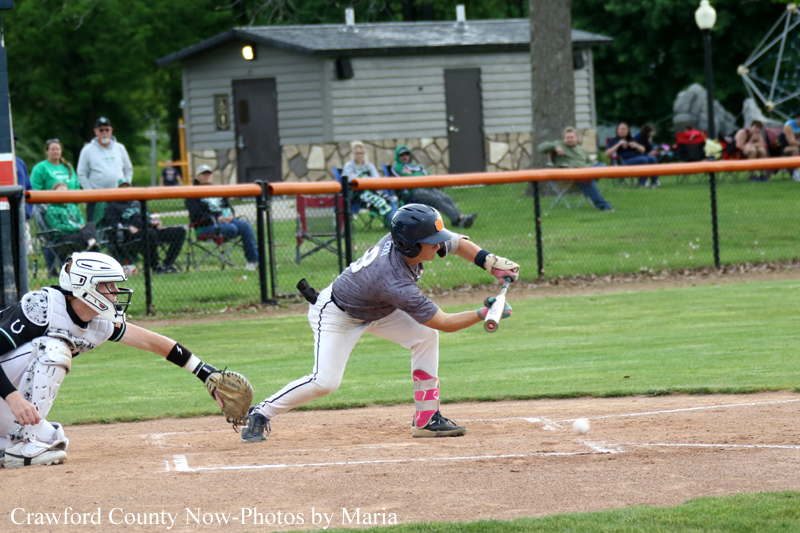 Baseball batter in gray swings at a pitch near home plate as the ball approaches; catcher crouches behind the plate in white gear.
