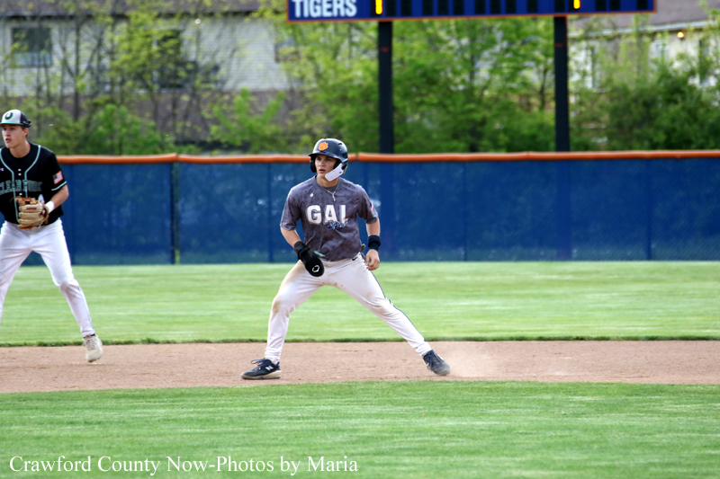 Baseball infield with a player in gray GAL jersey at a base, helmet on, glove ready, as a teammate stands in left field on a sunny day.