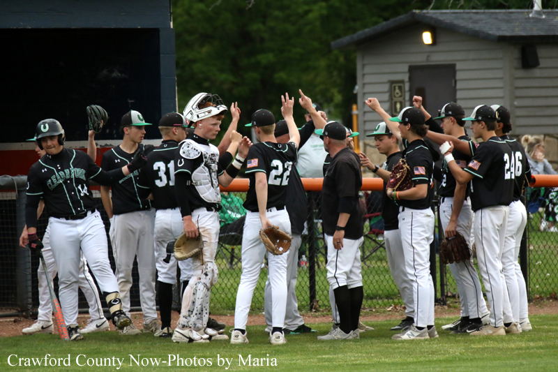 Baseball team in black uniforms high-fiving along the dugout fence after a game or practice.