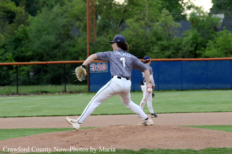Pitcher in gray uniform winds up on the mound for a throw during a baseball game, with a fielder in the background on green field.