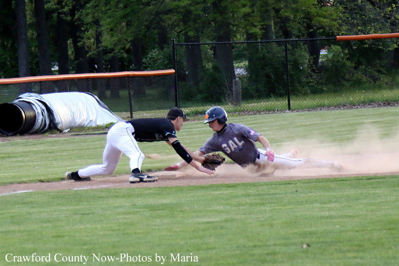 Baseball play: a runner slides into a base as a defender dives to tag him, dust kicking up on the infield.
