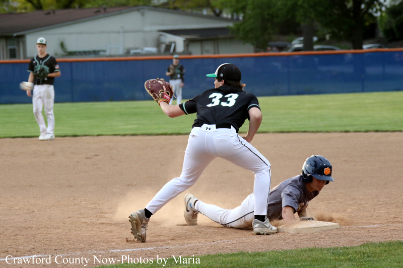 Baseball action: fielder in black jersey #33 ready with his glove near second base as a runner slides into the bag, dust rising on the dirt infield.