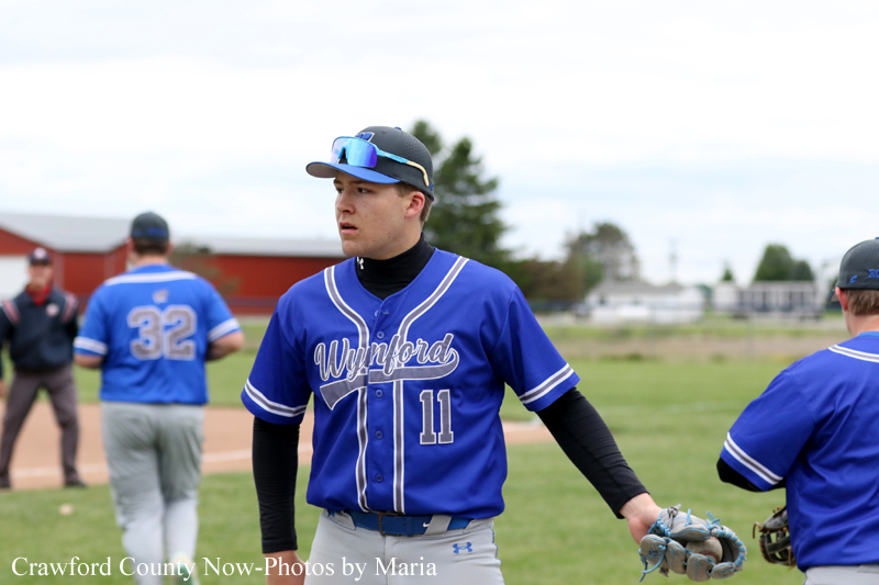 Baseball player in blue Wynford jersey #11 on the field, glove in hand, looking focused.