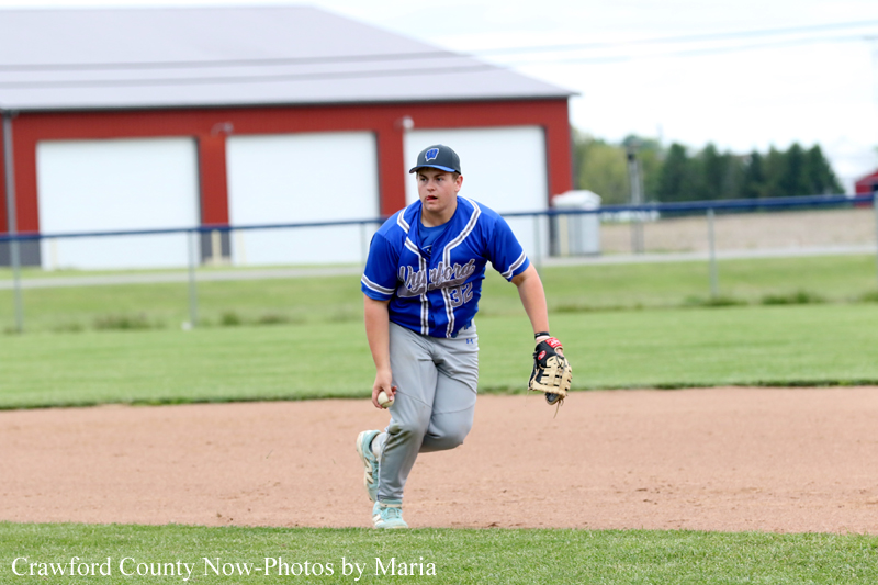 Baseball player in a blue uniform fielding a ground ball on the infield, glove on left hand.