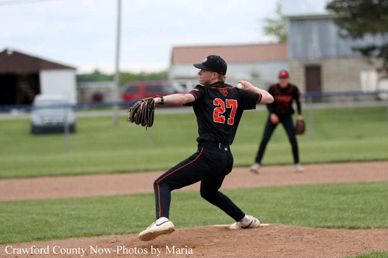 Baseball pitcher in black uniform with number 27 delivering a pitch on the mound, teammate in the background