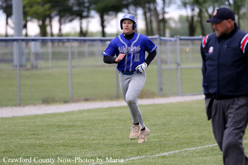 Young baseball player in a blue uniform (#11) running along a field, coach watching in the foreground.