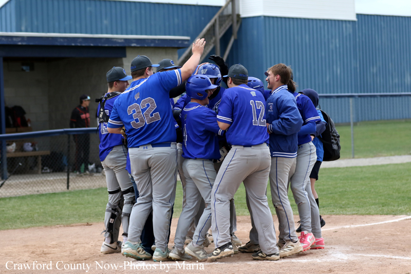 Baseball players in blue uniforms form a huddle on the infield dirt near the dugout, celebrating a moment together.