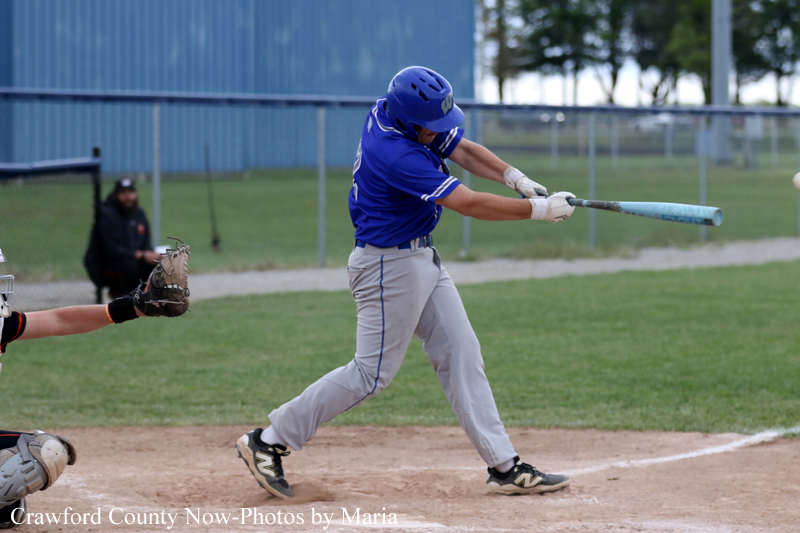 Baseball batter in a blue uniform swinging a bat during a game on a dirt field.