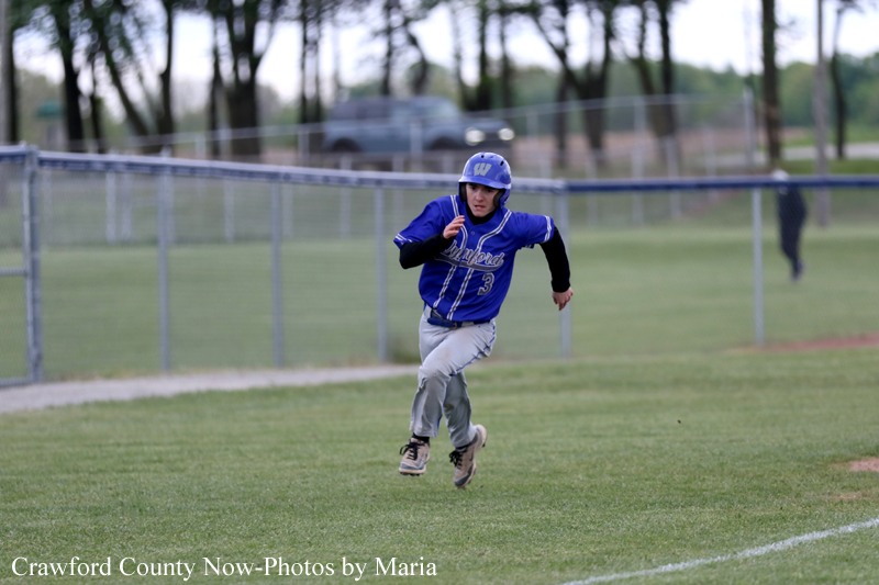 Youth baseball player in blue uniform rushing along a grassy field during a game in progress.