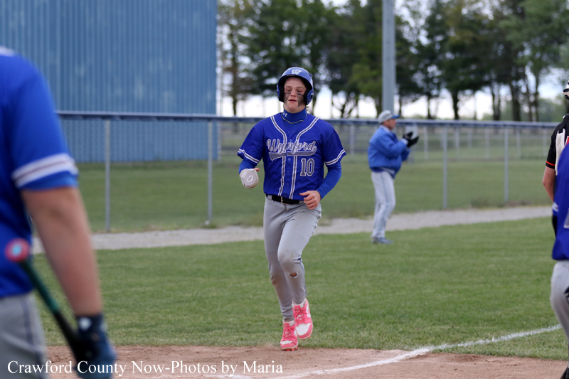 Baseball player in blue uniform (#10) running toward first base on a grassy field with a helmet on.
