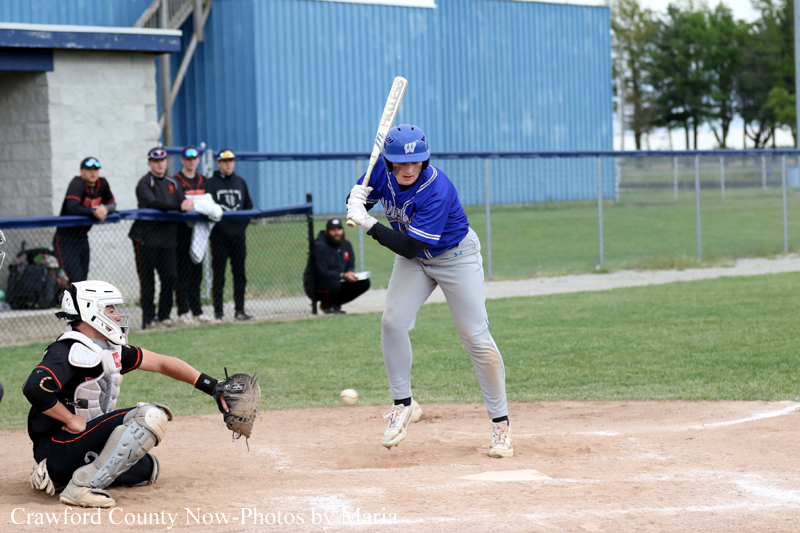 Baseball hitter in blue swings at a pitch while the catcher in black gear crouches behind home plate.