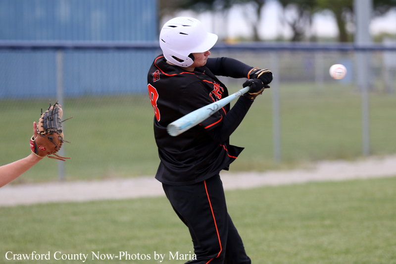 Baseball batter in a black uniform and white helmet swings at a pitched ball on a field.
