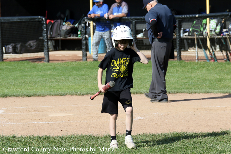 Young child in a helmet holding a bat on a baseball/softball field, about to swing during a game.
