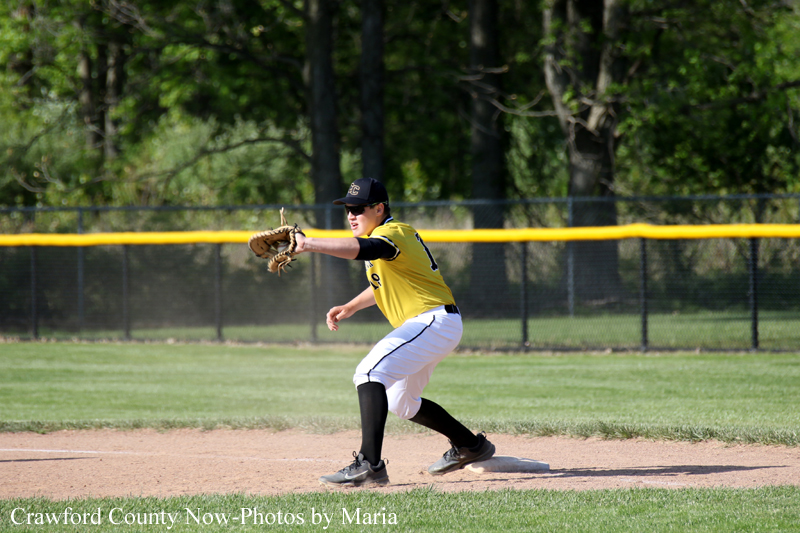Baseball infielder in a yellow uniform and black cap fields a ground ball on a dirt infield.