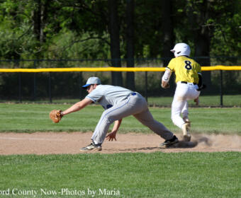 Baseball scene: fielder in gray dives to tag a ground ball as a yellow-clad runner (#8) slides toward the base, kicking up dust infield.