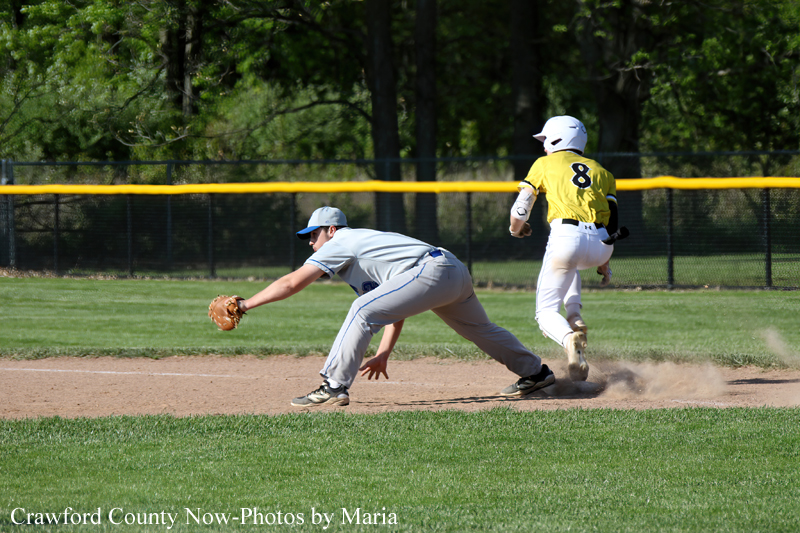 Baseball scene: fielder in gray dives to tag a ground ball as a yellow-clad runner (#8) slides toward the base, kicking up dust infield.