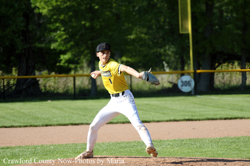 Young baseball pitcher in a yellow jersey delivering a pitch on the mound in a daytime game.