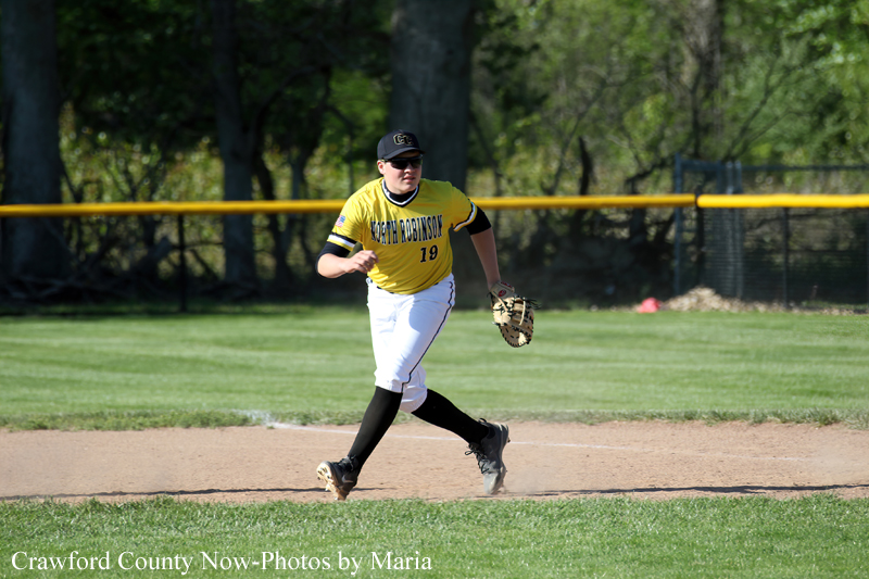Softball player in a yellow uniform with number 19 runs on the infield, glove on left hand, on a sunny day.