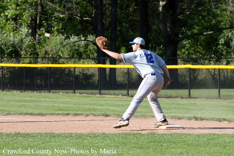 Baseball pitcher in gray uniform (number 12) winds up to throw from the mound on a sunny field.