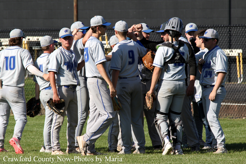 Youth baseball/softball team in gray uniforms huddling on the field before the game, wearing caps and gloves.