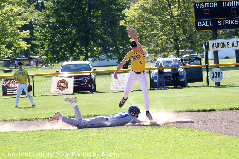 Baseball moment: fielder in yellow jumps as a baserunner slides into the base, dust puffing up on sunny infield.
