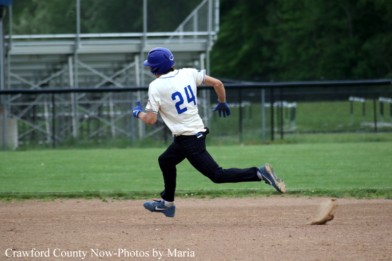 Baseball player in white jersey with number 24 running on infield dirt during a game, wearing a purple helmet and blue gloves.