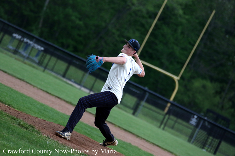 Baseball pitcher in a white jersey winds up on the mound, mid-throw with a glove up and cap on.