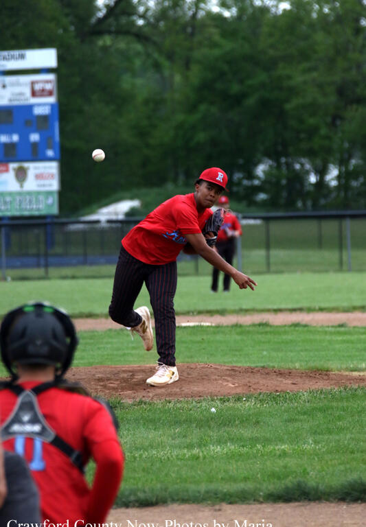 Baseball pitcher in red uniform mid-throw on the mound, catcher in foreground watching