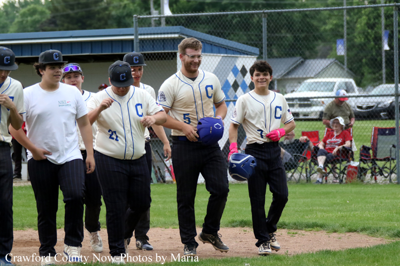 Youth baseball team walking off the field together, wearing cream jerseys with a blue ’C’ and numbers visible.