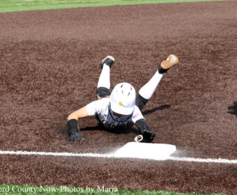 Player slides headfirst into a base, legs up in the air, reaching for the bag on a dirt infield during a softball game.
