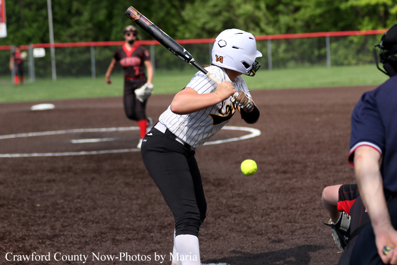 Female softball batter in a white helmet and pinstriped jersey swings at a pitch during a game on the infield.