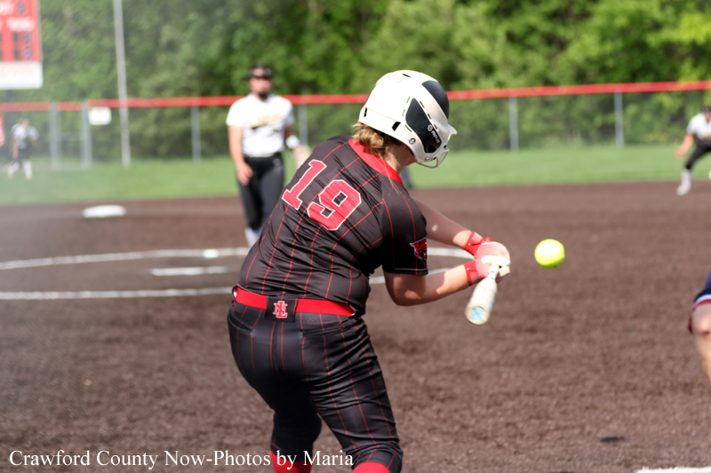 Softball batter in a black pinstriped uniform (number 19) swings at a pitch, wearing a white helmet on a dirt field.