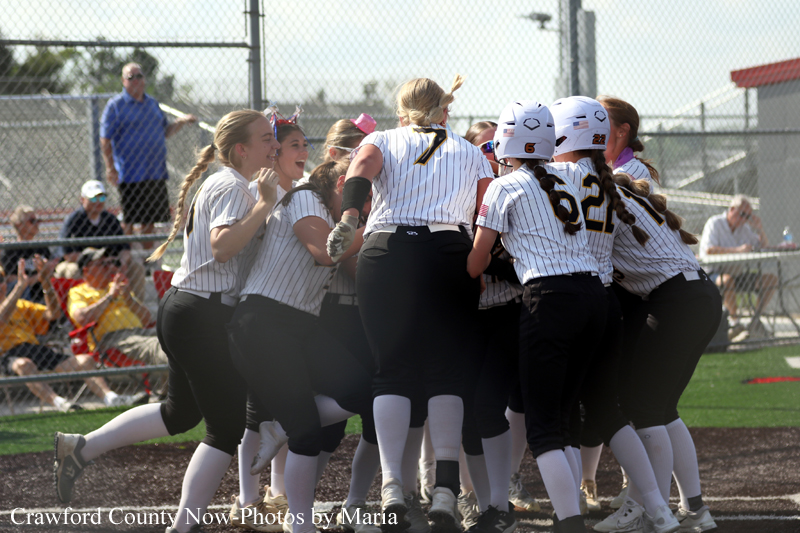 Girls' softball players in striped uniforms hug and Celebrate in a team huddle on the field.