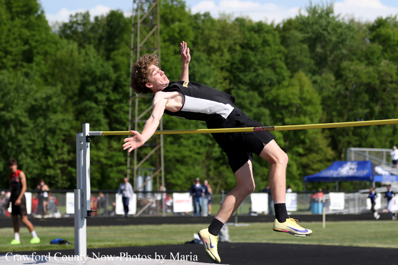 Male high jumper clears a yellow bar during an outdoor track meet, midair with back arched.