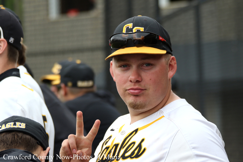 Baseball player in a white Eagles jersey faces the camera, making a peace sign with his right hand.